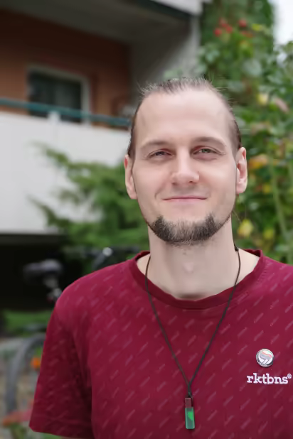 ich, lächelnd, mit zusammengebundenen Haaren, vor einem Strauch 